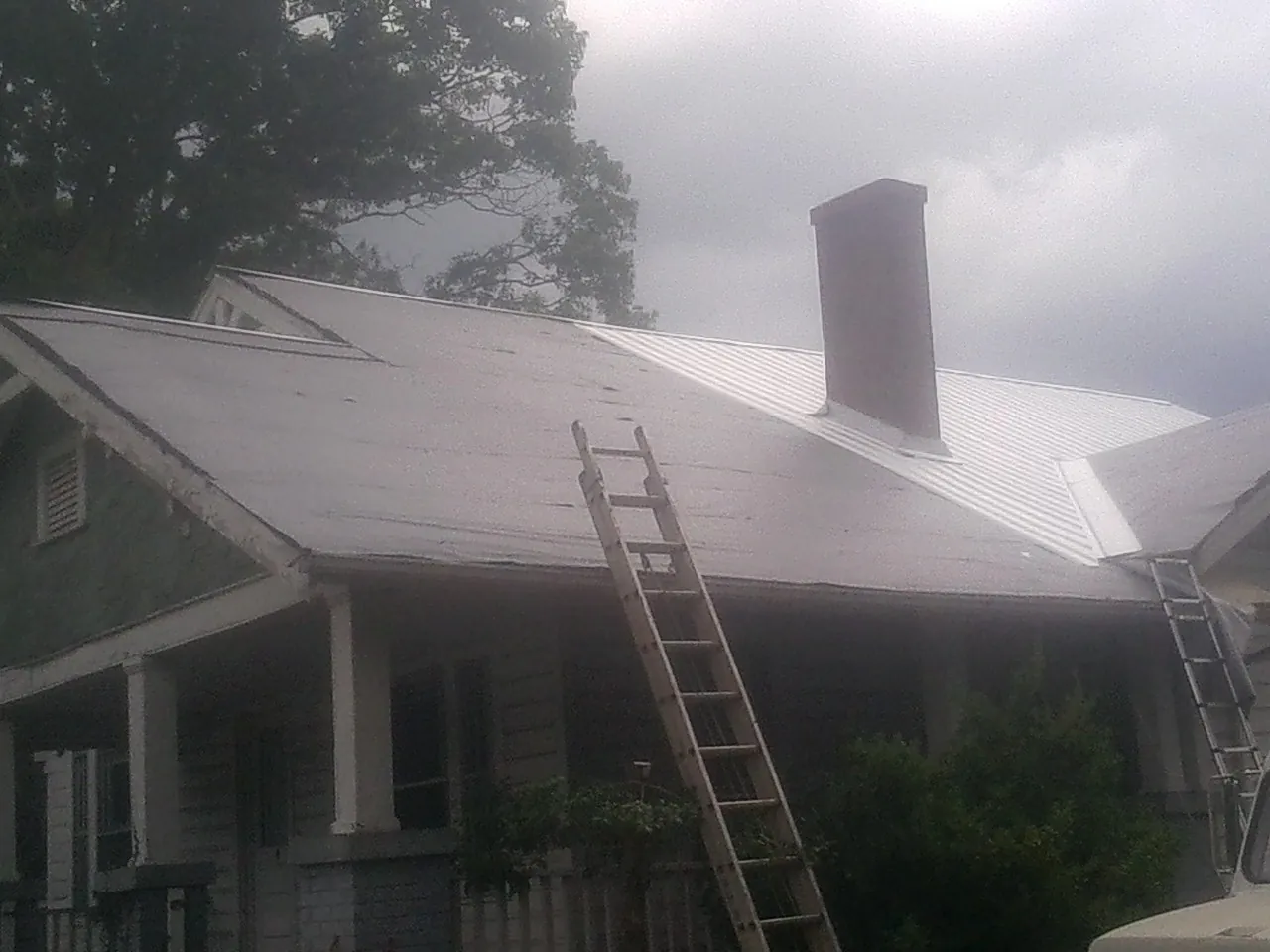 Ladders against a metal roof on an older home with a brick chimney in Clarksville